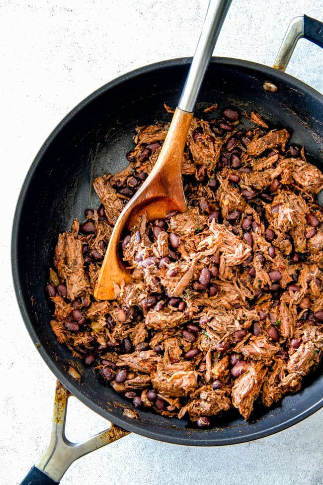showing how to make filling for beef enchiladas by mixing beef, black beans and enchilada sauce in a skillet with a wooden spoon