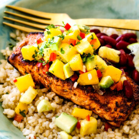 far away side view of cajun salmon in a green bowl with Pineapple, mango avocado salsa