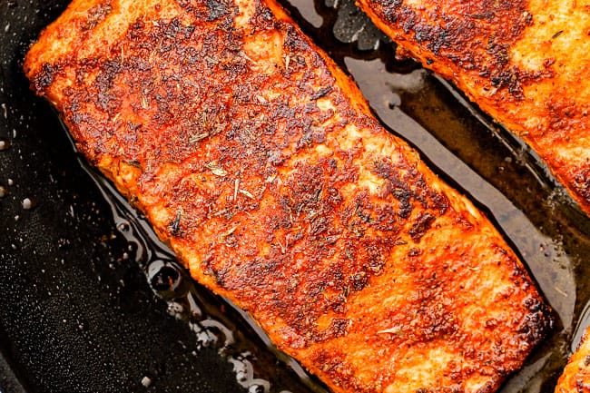 Cajun salmon in a black skillet being cooked