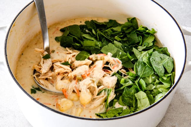 Showing how to make best Chicken Gnocchi Soup by adding spinach to soup with shredded chicken