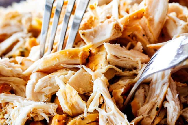 Showing how to make best Chicken Gnocchi Soup by shredding chicken on a cutting board with two silver forks to go back in soup