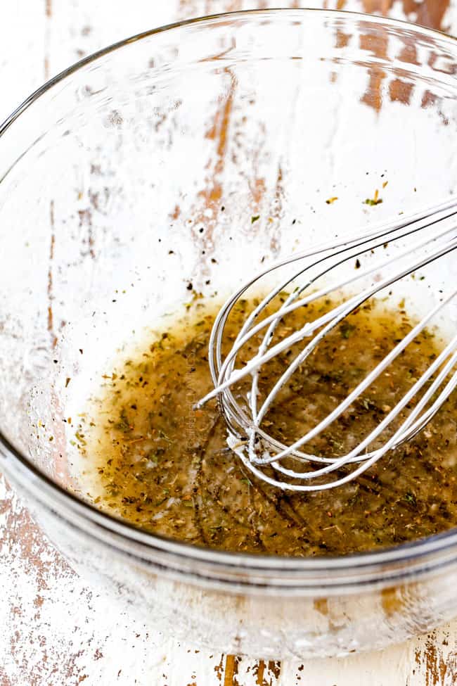 Whisking together Italian Dressing in a glass bowl for Cucumber Tomato Salad.