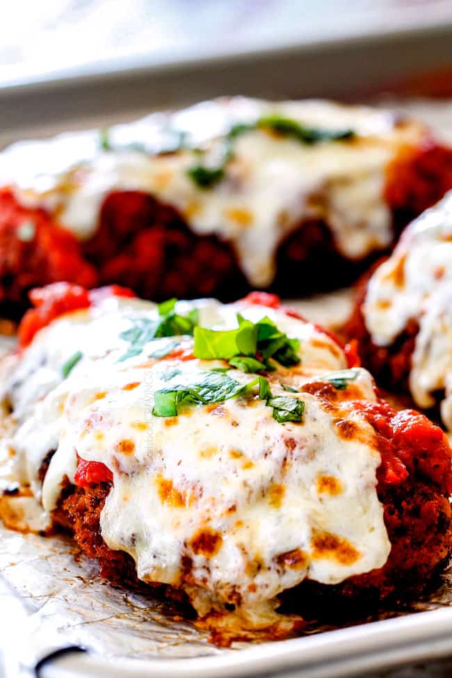 side view of baked Chicken Parmesan on a baking sheet with homemade marinara, mozzarella and basil