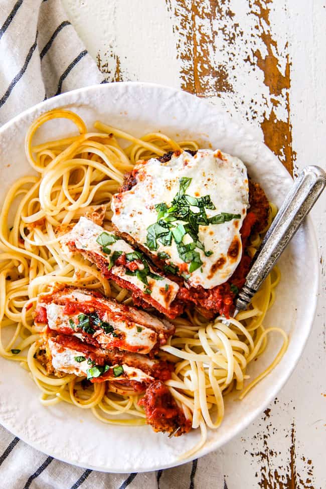 top view of easy chicken Parmesan partially sliced with spaghetti noodles in a white shallow bowl with fresh basil