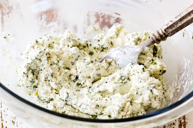 stirring together goat cheese with herbs in a glass bowls showing how to make cheese log