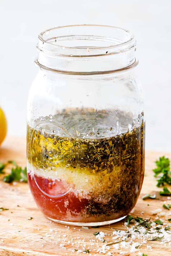 Showing how to make Homemade Italian Dressing recipe by adding vinegar, oil, garlic, lemon juice, basil, parsley, oregano, salt and pepper to a mason jar