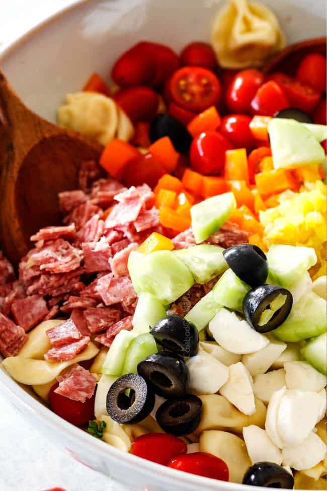 salami, tomatoes, bell peppers, mozzarella, cucumbers in a white bowl board for easy Italian Pasta Salad Recipe