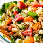 pasta, strawberries, spinach, Mandarin oranges, avocados, macadamia nuts in a glass bowl with poppy seed dressing mixed together for pasta salad