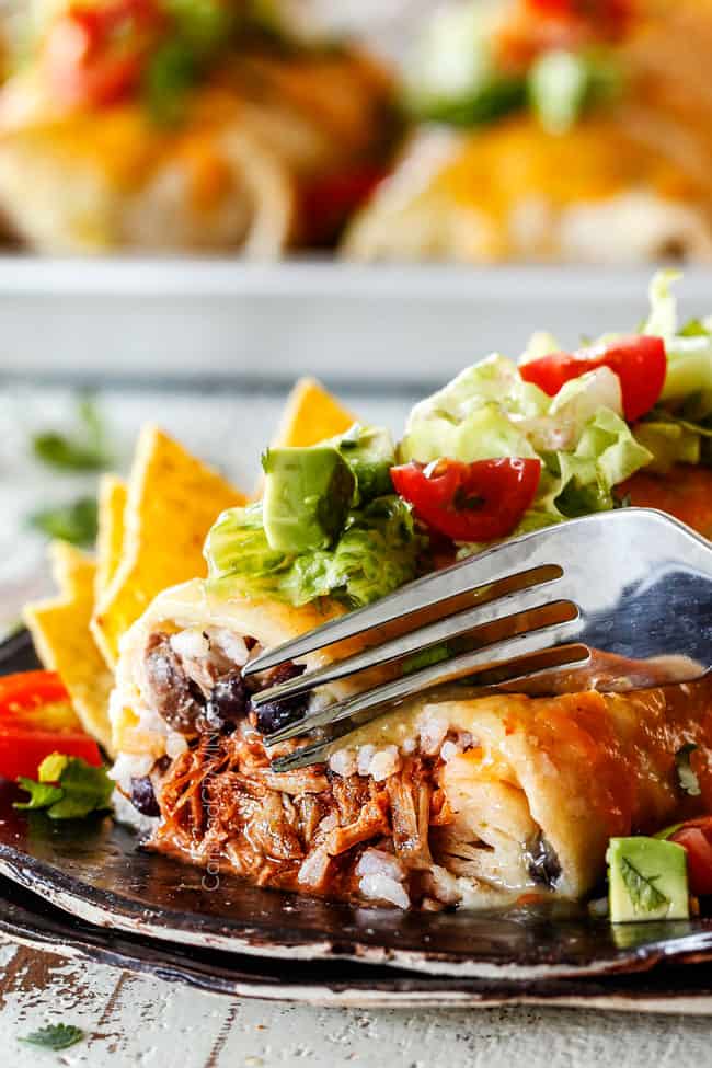Cutting into wet burrito with beef rice, black beans on a black plate garnished with lettuce, tomatoes, sour cream