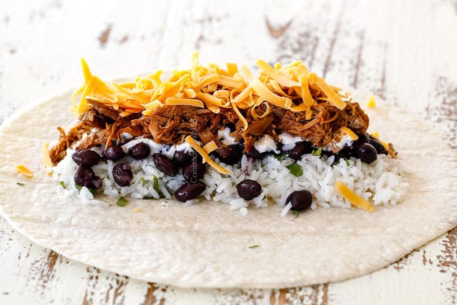 up close of tortilla layered with cilantro lime rice, black beans, sour cream, chipotle pork and cheese waiting to be folded into a burrito