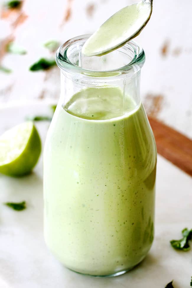 far away shot of spooning Cafe Rio Cilantro Lime Dressing out of a glass jar with a silver spoon