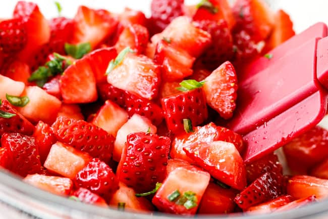 showing how to make Strawberry Goat cheese Bruschetta by mixing strawberries with basil in a glass bowl