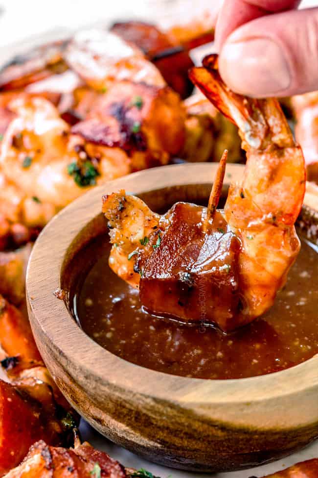 dipping grilled bacon wrapped shrimp in homemade cocktail sauce