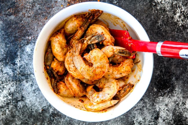 showing how to make bacon wrapped shrimp by marinating shrimp in a white bowl with garlic, lemon, olive oil, mesquite seasoining