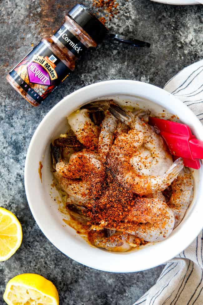 showing how to make bacon wrapped shrimp by marinating large raw shrimp in a bowl with mesquite seasoning, lemon juice, olive oil and garlic
