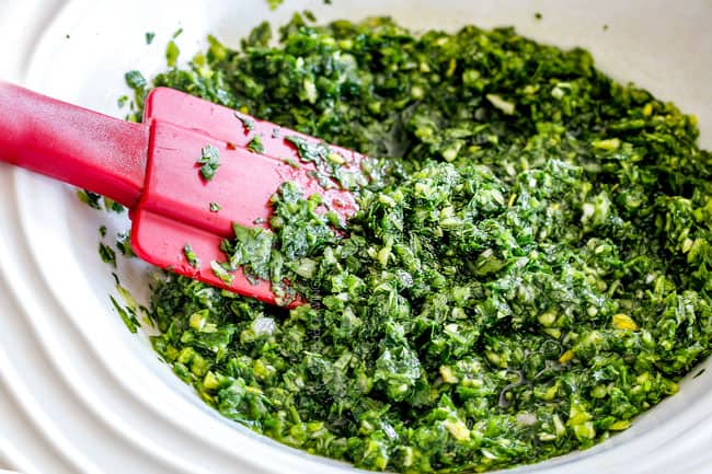 showing how to make chimichurri for Chimichurri steak by adding olive oil, red wine vinegar to cilantro and parsley in a white bowl