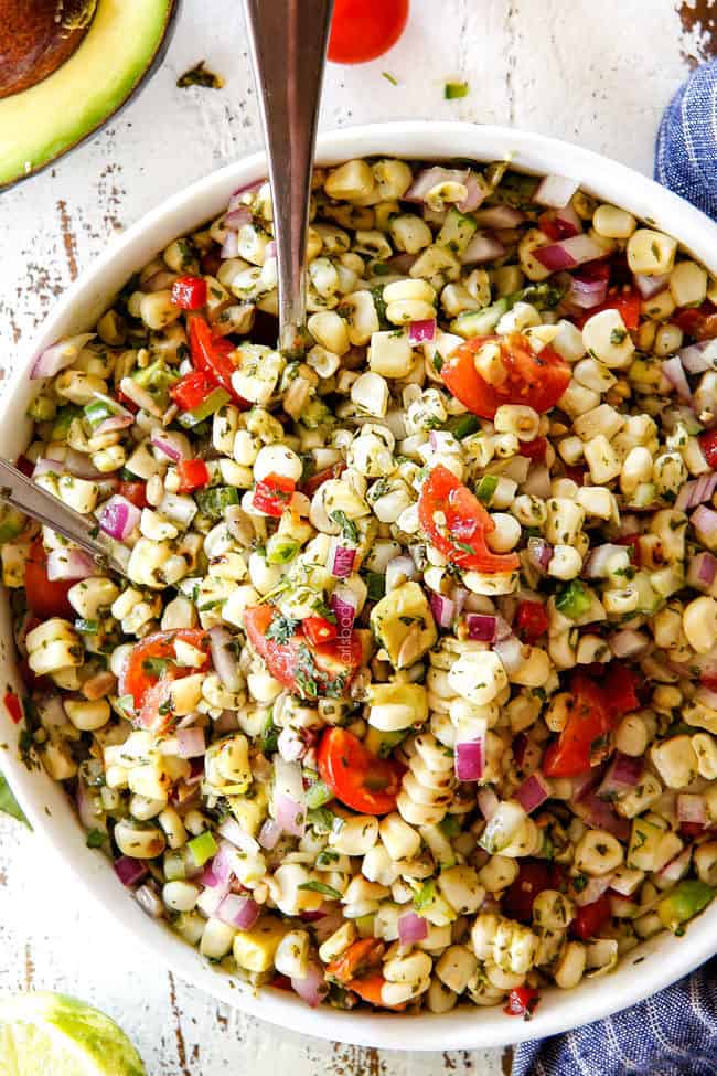 Fresh Corn Salad mixed together in a white bowl with silver spoons