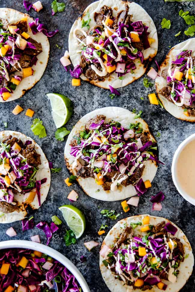 top view of 5 Korean tacos with steak laying flat on a grey surface with Gochujang Crema