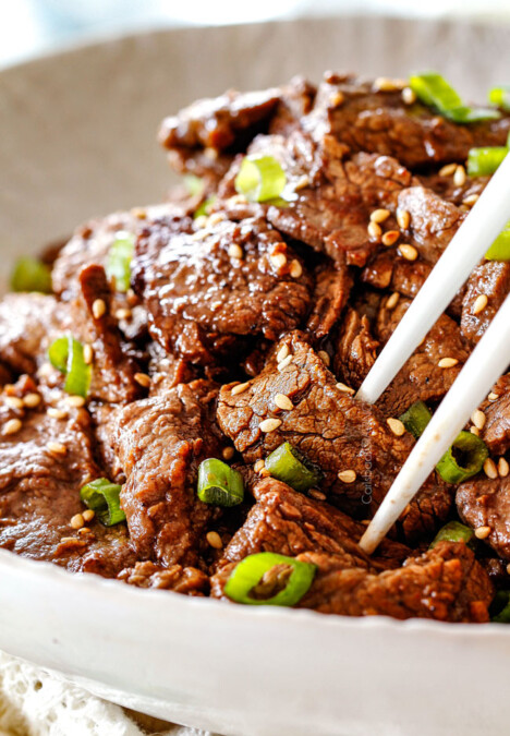 using chopsticks to pick up Beef Bulgogi in a white dish with sesame seeds and green onions