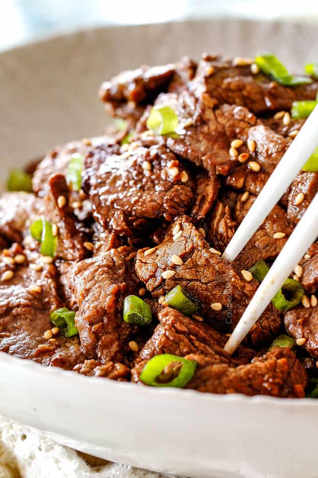 using chopsticks to pick up Beef Bulgogi in a white dish with sesame seeds and green onions