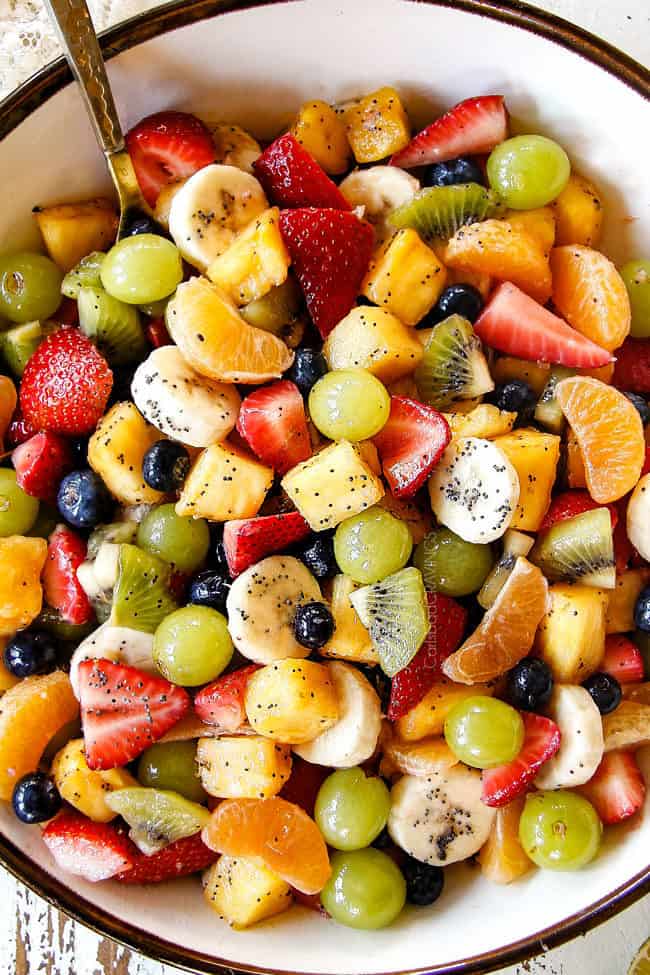 top view of best fruit salad in bowl with pineapple, strawberries, blueberries, bananas, kiwis, grapes and oranges