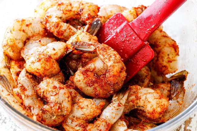 Showing how to make Shrimp Pasta salad by mixing raw shrimp with Cajun seasoning, olive oil and lemon juice