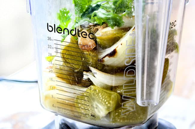 showing how to make salsa verde by adding tomatillos, cilantro, garlic, onions, seranos to blender