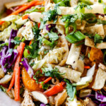 up close side view of top view of crunchy Chinese chicken salad with ramen noodles, Mandarin oranges, peanuts napa cabbage, wontons, carrots, snow peas, red bell peppers all tossed together with sesame dressing