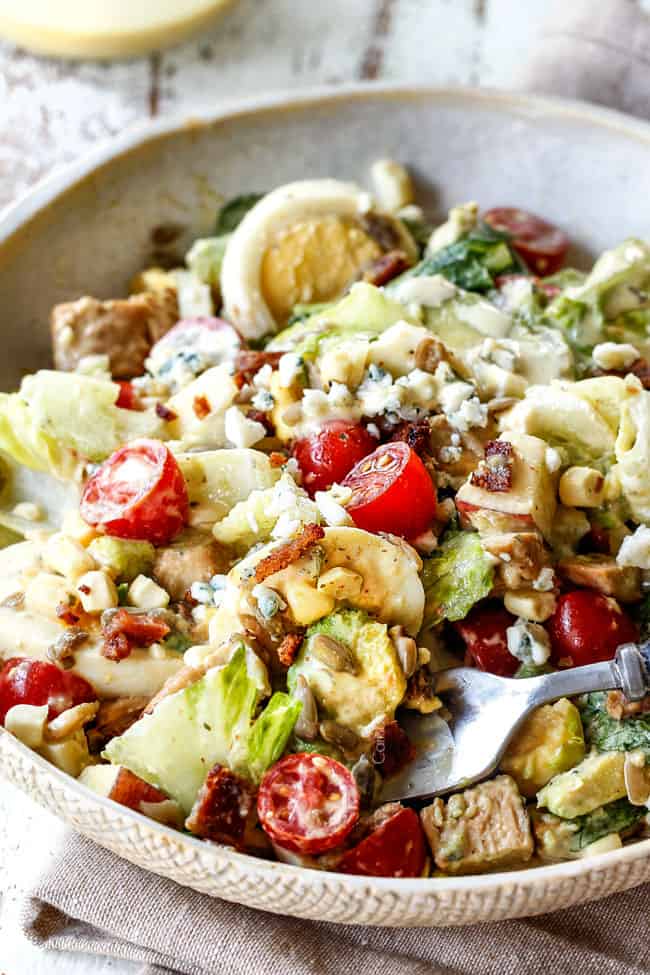 Cobb Salad on a plate with avocado, eggs, bacon, tomatoes, lettuce and blue cheese with a fork