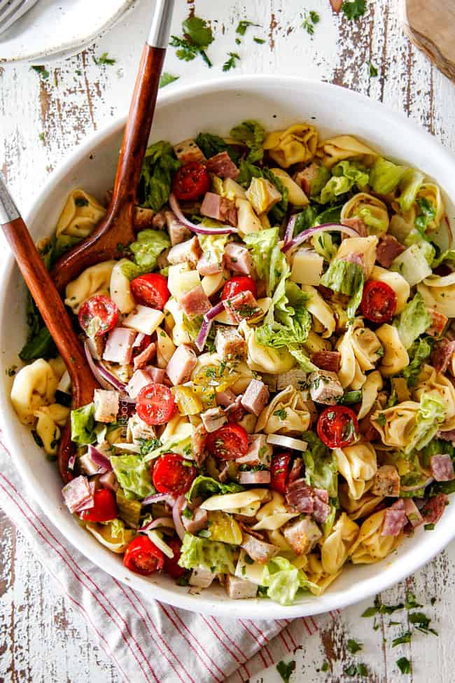 top view of pasta salad with cheesy tortellini, cubed pork roast, ham, salami, Swiss cheese, tomatoes, pickles pickled jalapenos, red onions, Romaine lettuce and cilantro
