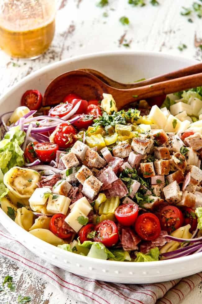 far away side view of Cuban pasta salad with cheesy tortellini, cubed pork roast, ham, salami, Swiss cheese, tomatoes, pickles pickled jalapenos, red onions, Romaine lettuce and cilantro