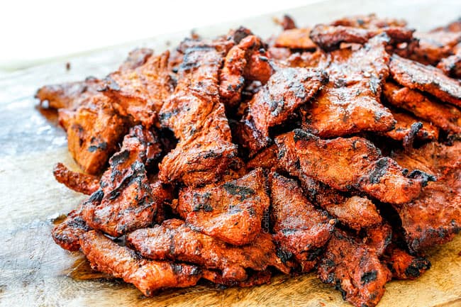 showing how to make Tacos Al Pastor with thinly sliced al pastor meat on a cutting board after it has been grilled