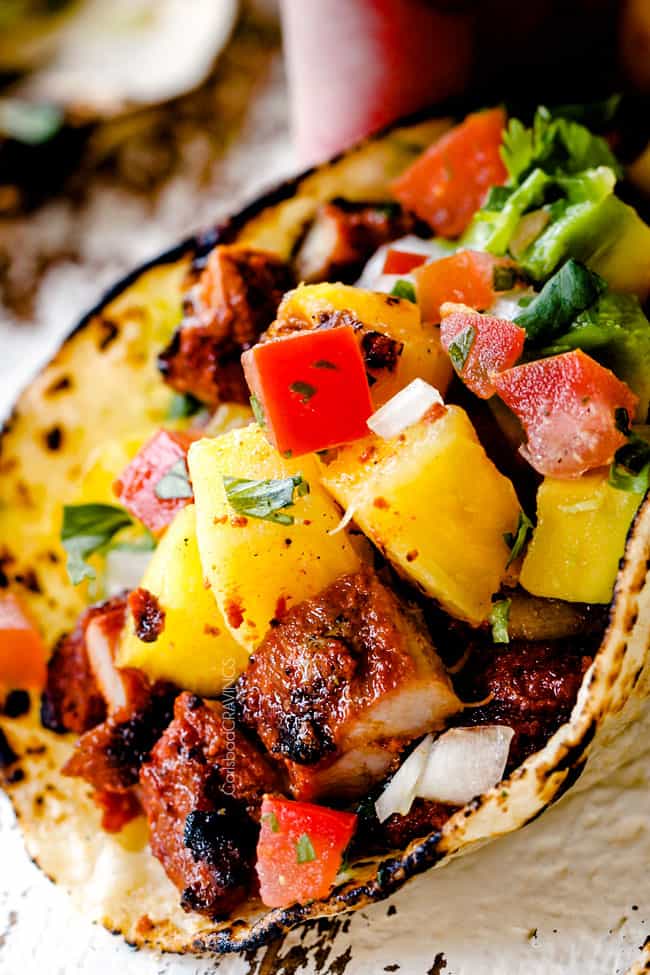 up close of Tacos Al Pastor with chopped al pastor, pineapple, pico de gallo and guacamole