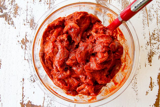 showing how to make tacos al pastor with thinly sliced pork in a glass bowl covered in bright red mariande