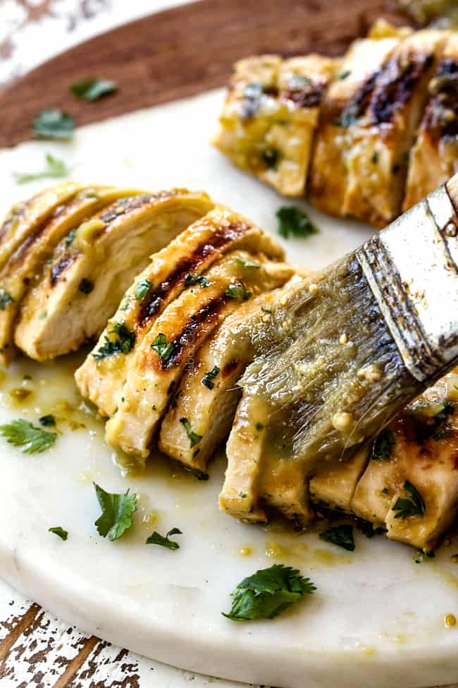 brushing salsa verde chicken with salsa verde after it is cooked