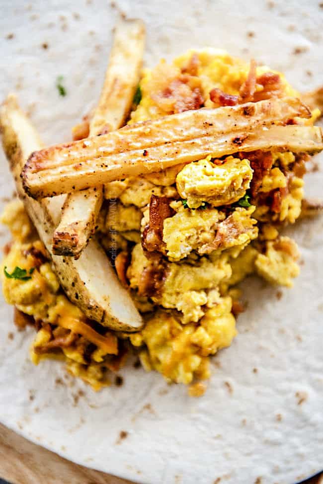 showing how to make easy breakfast burritos by piling a tortilla with eggs, cheese, bacon and french fries