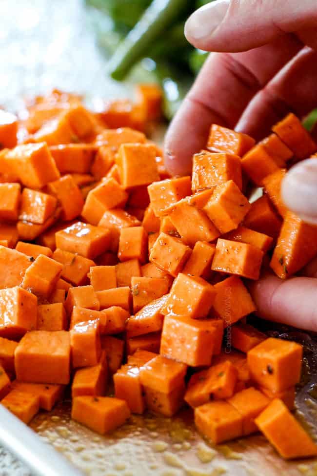 showing how to make sheet pan chicken with potatoes by tossing sweet potatoes in some reserved marinade