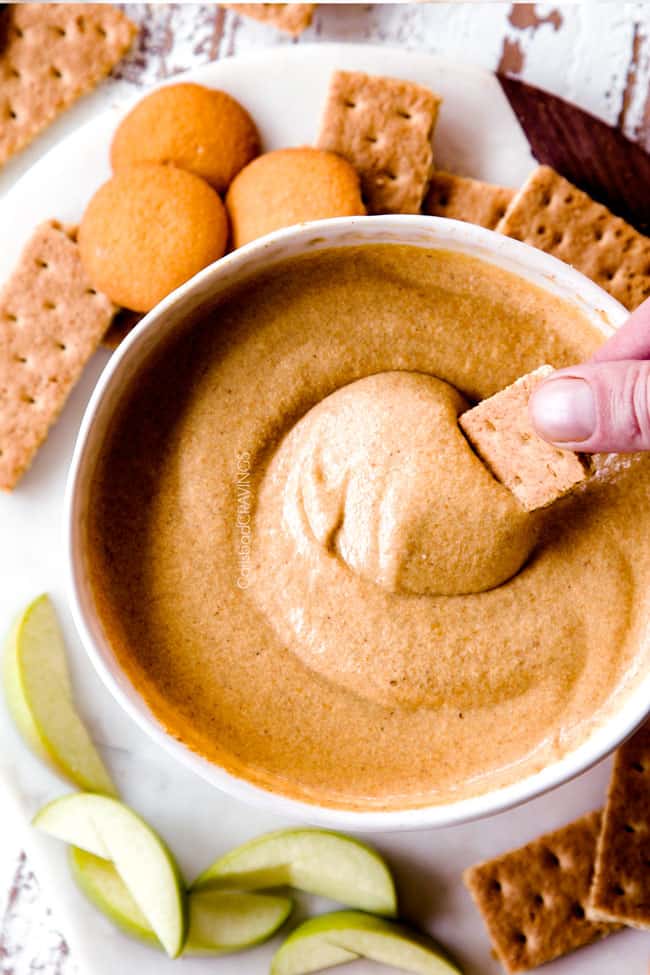 top shot dipping a graham cracker into no bake pumpkin dip