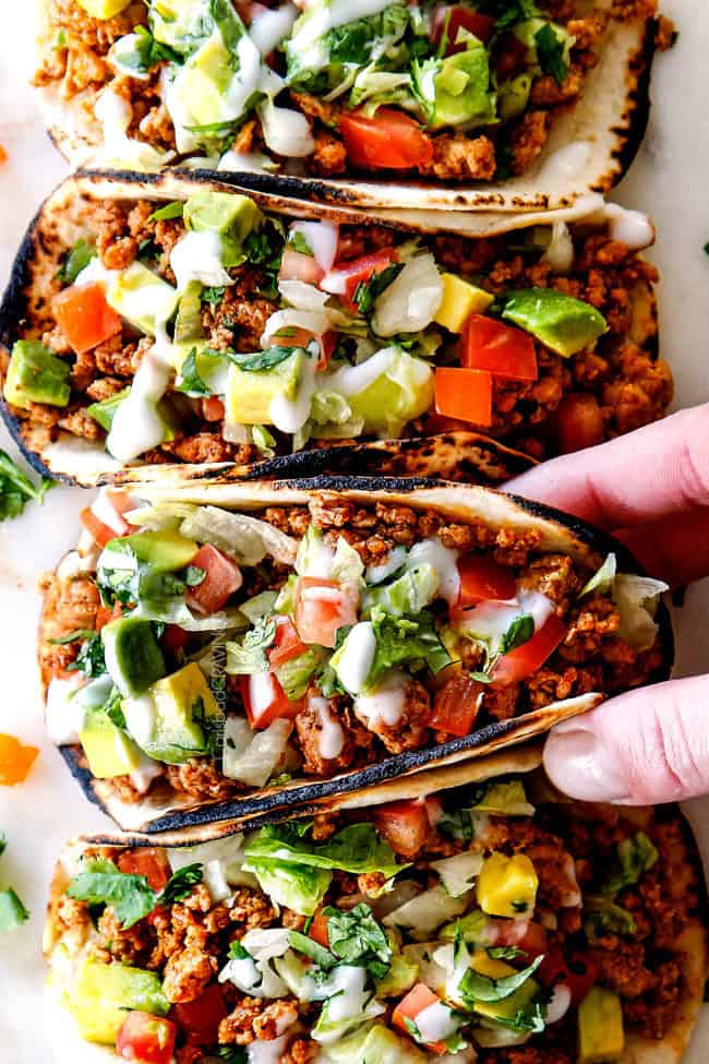 up close top view of a row of easy turkey taco with ground turkey, taco seasoning, lettuce, sour cream, tomatoes and avocados