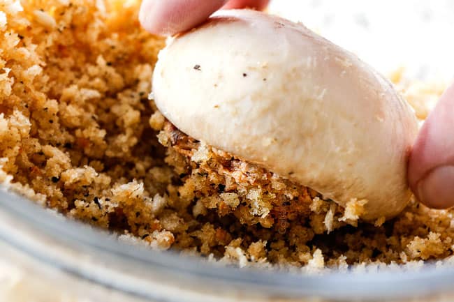 showing how to make sausage stuffed mushrooms by dipping stuffed mushrooms in panko topping