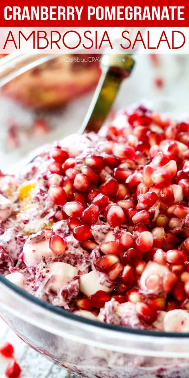 up close of a spoon scooping classic ambrosia salad with pineapple, mandarin oranges, mini marshmallows, cranberries and pomegranate seeds in a glass bowl