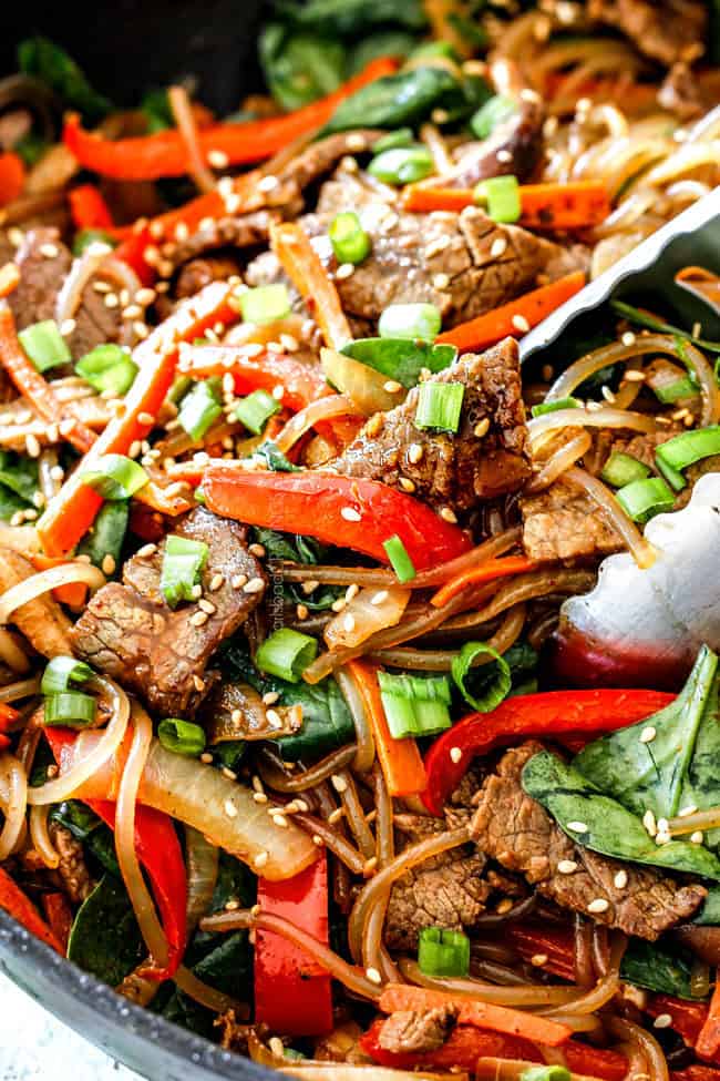 up close of a pair of tongs grabbing a bite of Spicy Korean Noodles