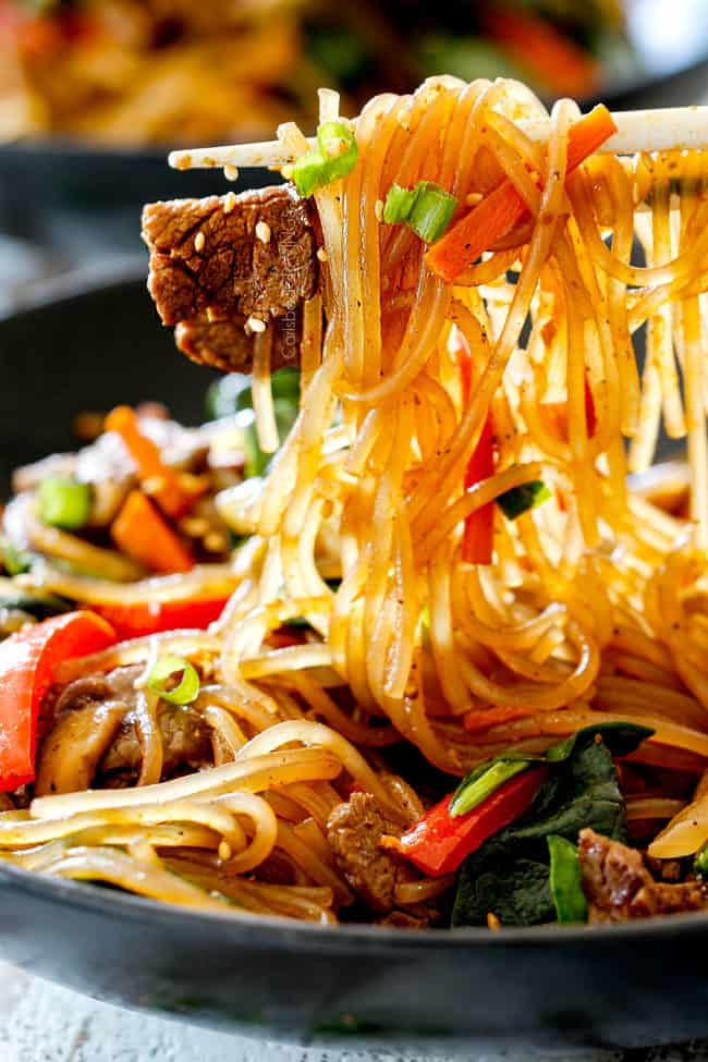 a pair of chopsticks holding up Spicy Korean Noodles with steak