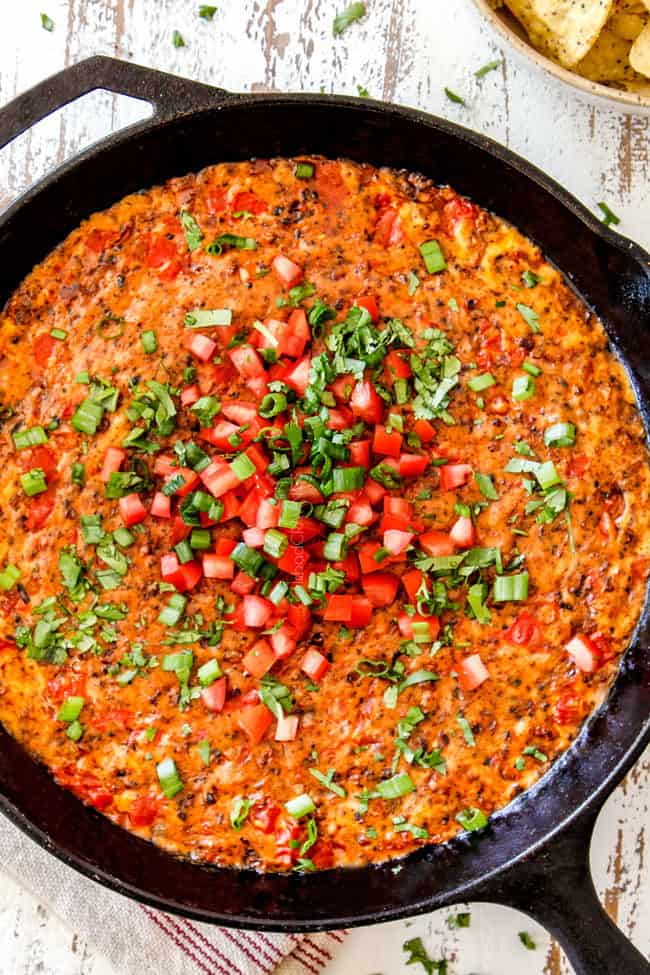 top view of best queso fundido in a cast iron skillet garnished with tomatoes, cilantro and green onions