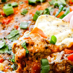 up close of a tortilla chip dipping into Queso Fundido with gooey melty cheese