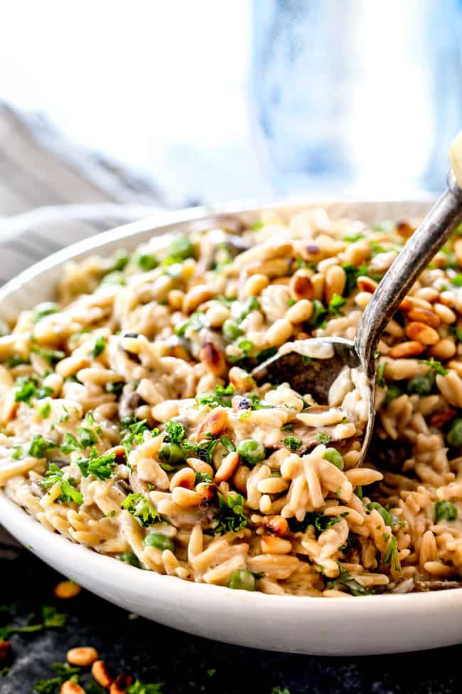 side view of cheesy orzo pasta recipe with a serving spoon with mushrooms and peas