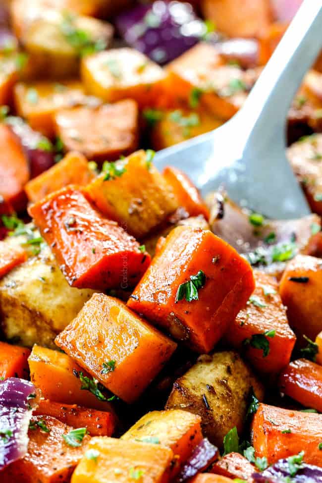 up close of a spatula scooping up balsamic roasted root vegetables with garlic on a baking tray