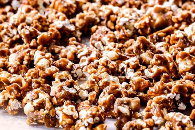 showing how to make caramel popcorn by spreading baked popcorn out on parchment paper