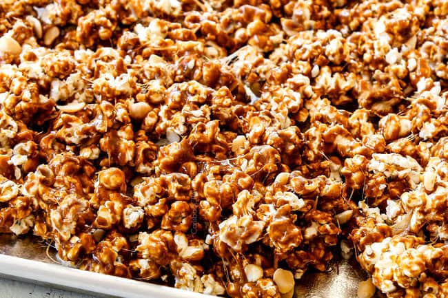 up close of showing how to make caramel popcorn by spreading caramel covered popcorn out onto a baking sheet