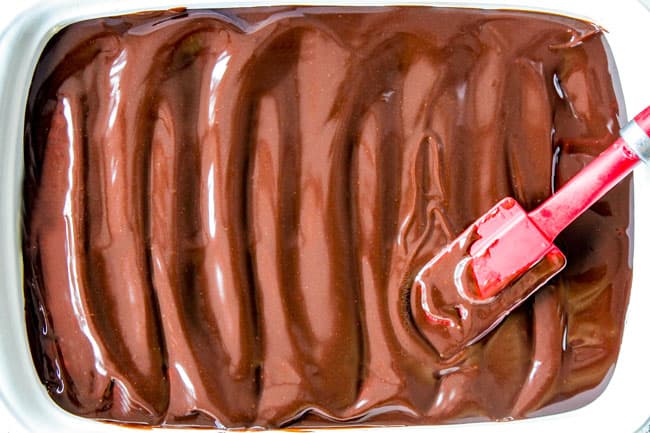 showing how to make best Chocolate Eclair Cake by spreading chocolate frosting on top of graham crackers